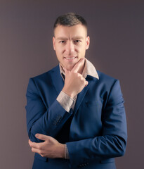 Young male businessman in a blue suit is thinking on a dark background