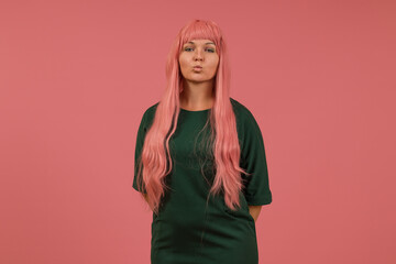 a pretty young woman with long pink hair and a green dress folded her lips in a kiss on a pink...