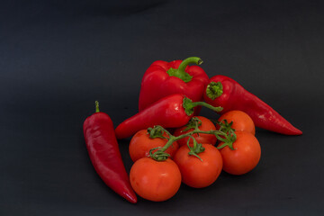 Red vegetables on a black background. Peppers and tomatoes, garlic