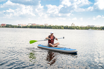 beautiful young woman in a protective vest learns to swim on a sup board on a city lake