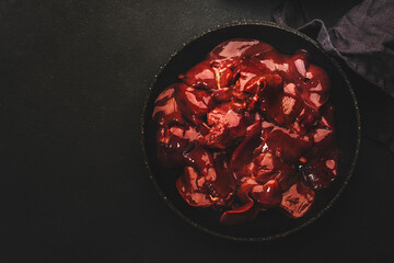 Fototapeta premium Fresh raw chicken liver in frying pan and ingredients for cooking on concrete black stone kitchen table, top view, copy space