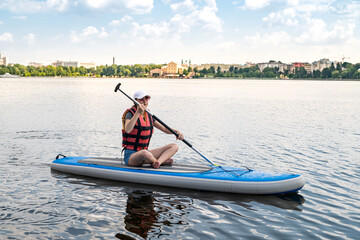 Young woman sitting on paddle board wear life vest