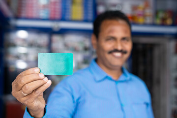 smiling medical owner showing green screen empty card by looking at camera at pharmacy - concept of employee id, advertisement and retail medical shop