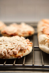 Small frozen pizza semi-finished product with tomato sause and cheese on grill prepared for baking. Selective focus