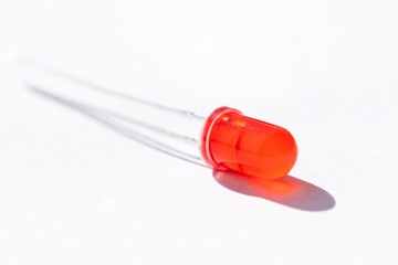 A close up studio portrait of a single red LED or colored Light Emitting Diode lying on a white background, ready to be used in some kind of electronics PCB or circuit or print board.