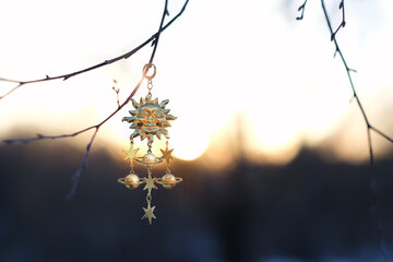 Solar golden amulet on branch, natural sunny blurred background. Sun symbol of spring equinox,...