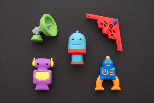 Flat lay of cute AI robots and advance technology eraser toy set on black background minimal style. Kids imagination, learning, back to school and education concept.