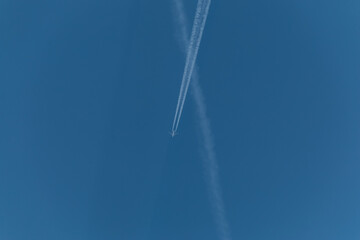 The plane flies through the clear blue sky with long vapor trails. With copy space to add text.