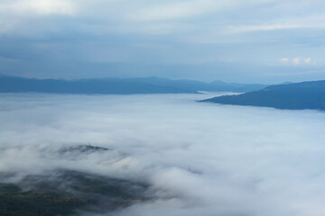 The hollow is covered with fog. In the background are mountain ranges and a cloudy sky. Beautiful landscape with fog.