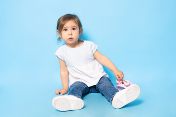 2 years old child sitting on the floor with an alarm clock over blue background.