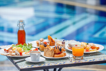 Close up of breakfast at European style hotel by the swimming pool. Table with delicious food by...