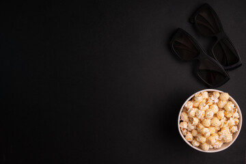 bucket of caramel popcorn and glasses for 3d movies on a black background top view. The concept of...