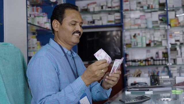 Happy pharmacist couting money at counter - concept of successful business, earnings or profit and retail medical shop.