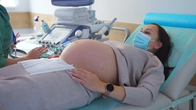 Last months pregnant woman at doctor's check up. Dark haired lady lies on the couch of obstetrician near ultrasound apparatus.