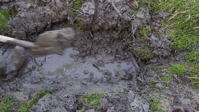 A man in rubber boots clears a channel for water flow with a shovel.