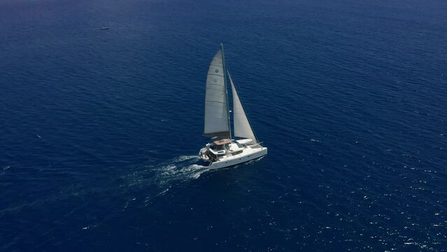 Aerial footage, rear view of luxury sailboat sailing on a deep blue sea with white wakes. Camera follow catamaran in blue ocean water