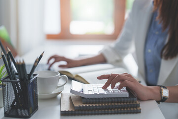 Asian Business Woman or Accountant do math and analyze with calculator and paperwork on desk,...