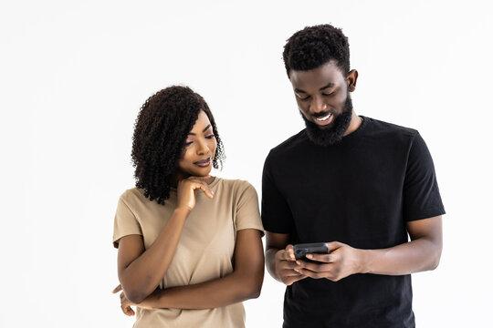 Attractive african couple hold smart phones having fun in internet, guy help explain to girl new cool free online application, point finger show to photos, isolated on gray studio background