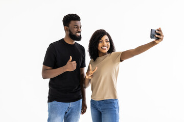 Young african couple taking selfie on a mobile phone on white wall background.