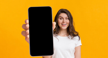 Positive lady showing big cellphone with blank screen, demonstrating space for your website or app...