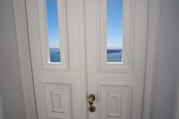 Fototapeta premium A typical white traditional door, the blue sky , the aegean sea and the volcano of Santorini in the background