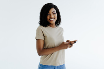 Young african woman in blank white t shirt, isolated on gray background, texting or browsing with happy relaxed smile