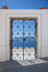 An external decorated door with flower plants on the roof of a villa and  view of the aegean sea in Fira Santorini