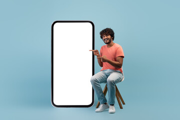 Positive indian guy in casual sitting by huge cell phone