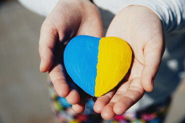 Small little kid hold heart shaped stone with Ukraine blue-yellow national flag or anthem. Girl...