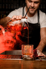 bartender holds mixing cup with red cocktail and pours it into a glass