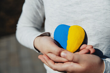 Small little kid hold heart shaped stone with Ukraine blue-yellow national flag or anthem. Girl...