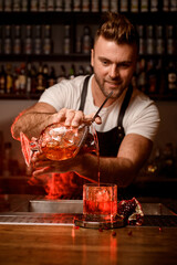 bartender holds mixing cup with a cocktail and pours a drink into a glass