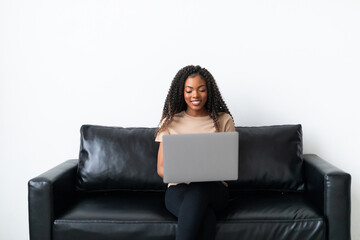 Attractive young African woman working on laptop and smiling while sitting on the couch at home