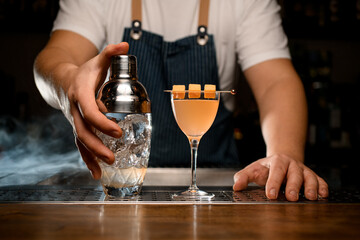 Male hand holds crystal glassy shaker with ice. Cocktail glass with drink on bar counter