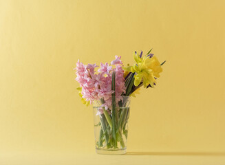 Spring flowers in a glass with water. Yellow background. Spring concept