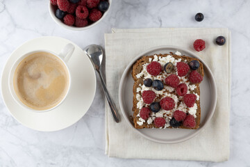 Whole grain bread toasts with cottage cheese and fresh raspberries ,blueberries and with flax seeds with cup of coffee , on a white background .Top view .Dieting concept .