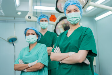 Fototapeta na wymiar Portrait of Asian women surgeon and nurse with medical mask standing with arms crossed in operation theater at a hospital. Team of Professional surgeons. Healthcare, emergency medical service concept