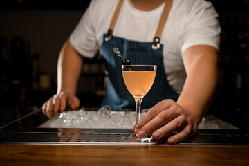 hand of bartender holds cocktail glass with alcoholic drink decorated with berry