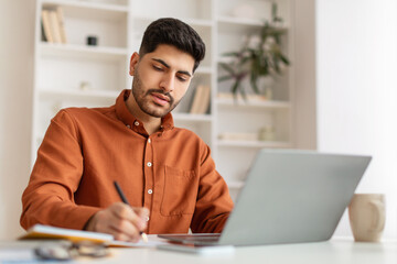 Portrait of focused Arab man using pc and writing