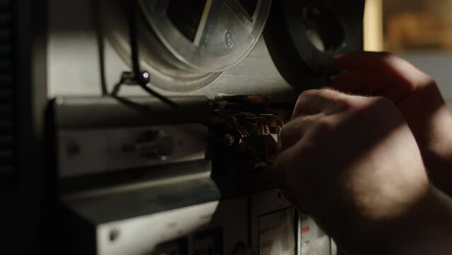 close up view of man's hands refilling magnetic tape on old reel-to-reel tape recorder. vintage tape recorder is tuned to play reel on it. concept of preparation for film.