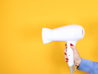 Fototapeta premium Hand holding white Hair dryer on yellow background. Beauty concept. Modern equipment for a hairdresser.