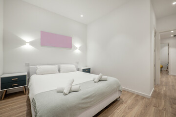 Bedroom with a double bed with a gray blanket and rolled towels, a built-in wardrobe, black side tables and a wooden floor in a vacation rental apartment
