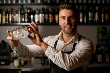 smiling male bartender holding a glass shaker in his hands