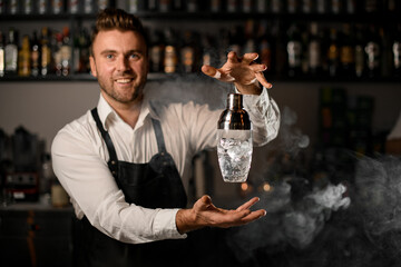magnificent view of the glassy shaker in the air and the hands of male bartender near it.