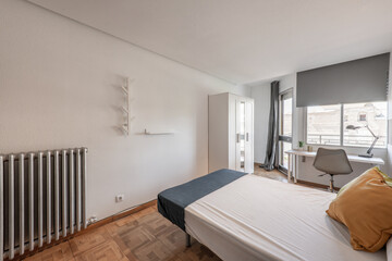 Bedroom with single bed, cast iron radiator, white desk by the window and oak parquet flooring