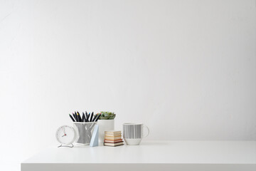 White desk with supplies, mug and white wall copy space. Home business workspace.