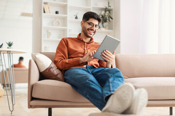 Smiling young Arab man using digital tablet at home - Powered by Adobe