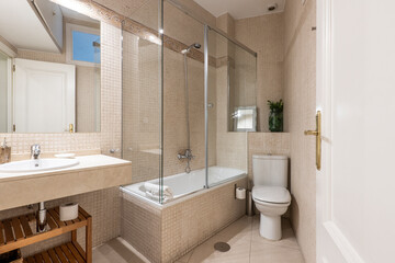 Bathroom with white porcelain sink on cream marble top, frameless mirror and shower stall with sliding glass door