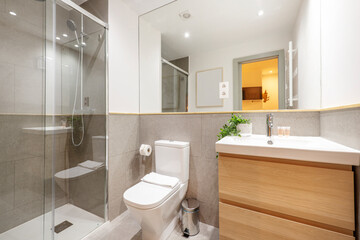 Bathroom with white porcelain sink on wooden cabinet with drawers, frameless wall-to-wall mirror and glass-enclosed shower stall
