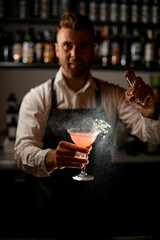 cocktail glass with drink bartender holds in his hand and sprinkles on it